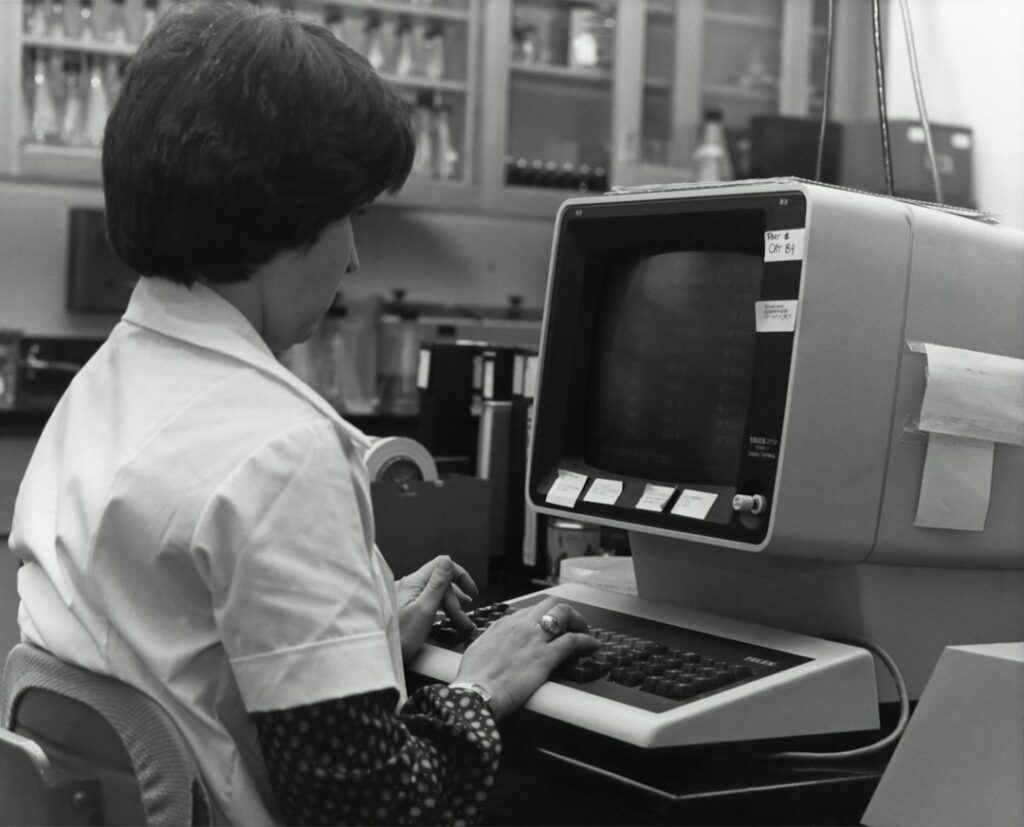 Mulher trabalhando com computador antigo, remetendo à história da programação