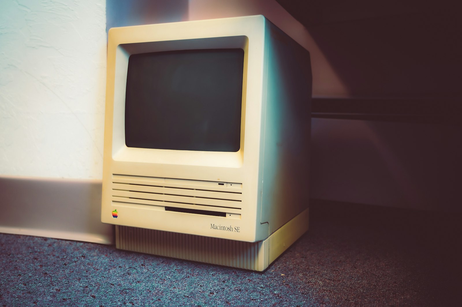Um Macintosh SE antigo e esquecido embaixo de uma mesa de biblioteca